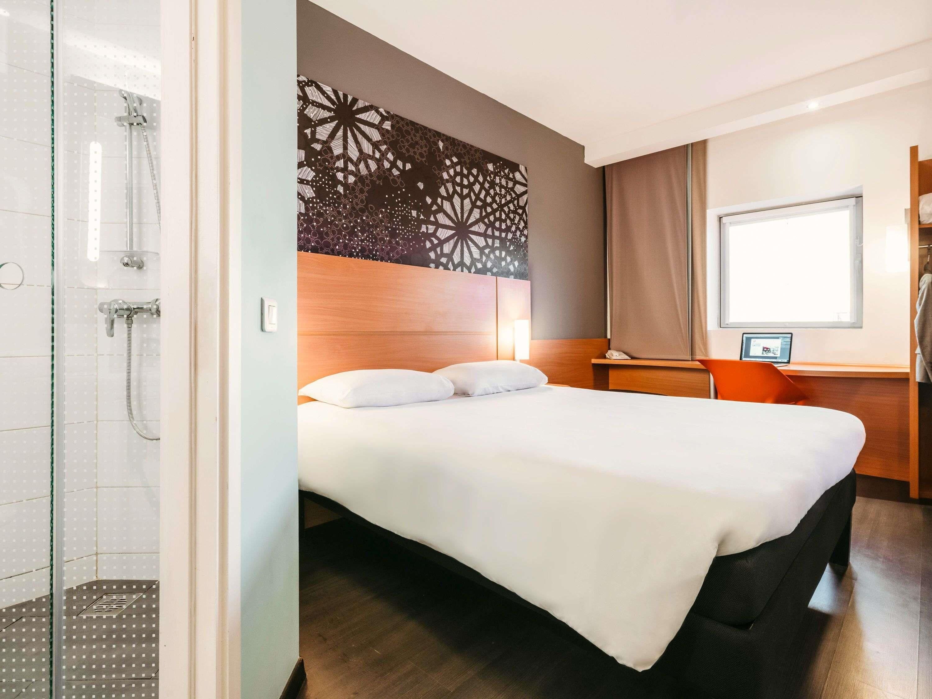 A hotel room with a bed, a shower, a desk with a computer, and a window.