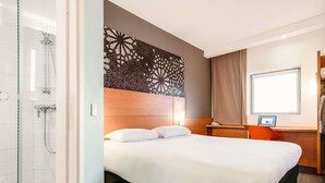 Habitación de hotel con cama, ducha, escritorio y ordenador, además de ventana.