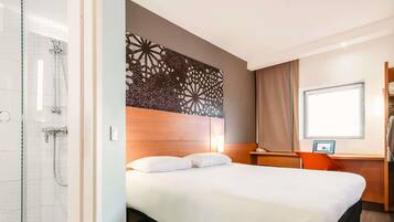 A hotel room with a bed, a shower, a desk with a computer, and a window.