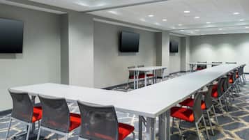 A conference room with a long white table, red chairs, and two flat-screen TVs mounted on the walls.