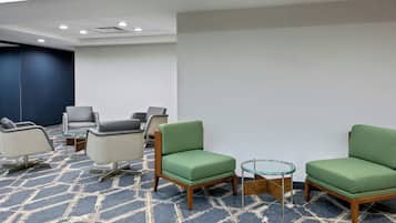 A hotel lobby with a blue patterned carpet, several chairs, and a glass coffee table.