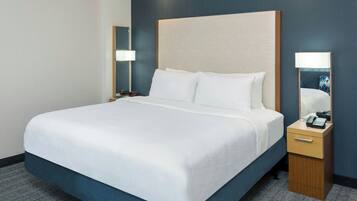 Una habitación de hotel con una cama grande, una mesita de noche, una lámpara y un espejo.