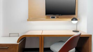 A modern office desk with a mounted flat-screen TV, a desk lamp, and a cushioned chair.