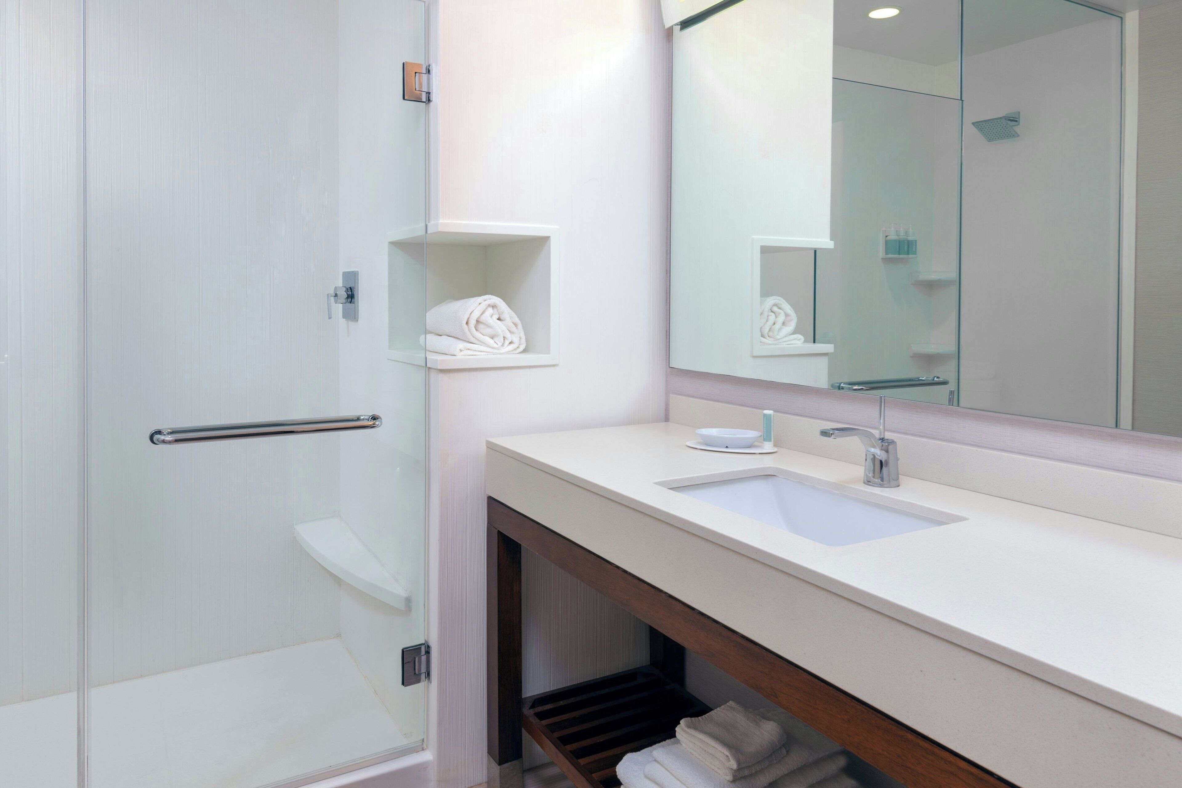 Un baño moderno con cabina de ducha de vidrio, un lavamanos blanco y un espejo sobre él.