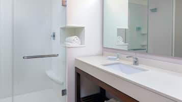 Un baño moderno con cabina de ducha de vidrio, un lavamanos blanco y un espejo sobre él.