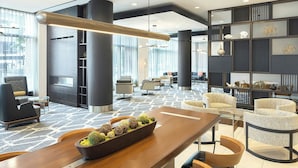 Un hall d’entrée moderne avec un comptoir d’accueil en bois, des sièges confortables et un mur décoratif agrémenté d’étagères.