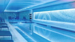 Une piscine intérieure moderne, dotée d’une eau claire, de chaises longues et d’un grand mur orné d’un motif texturé.
