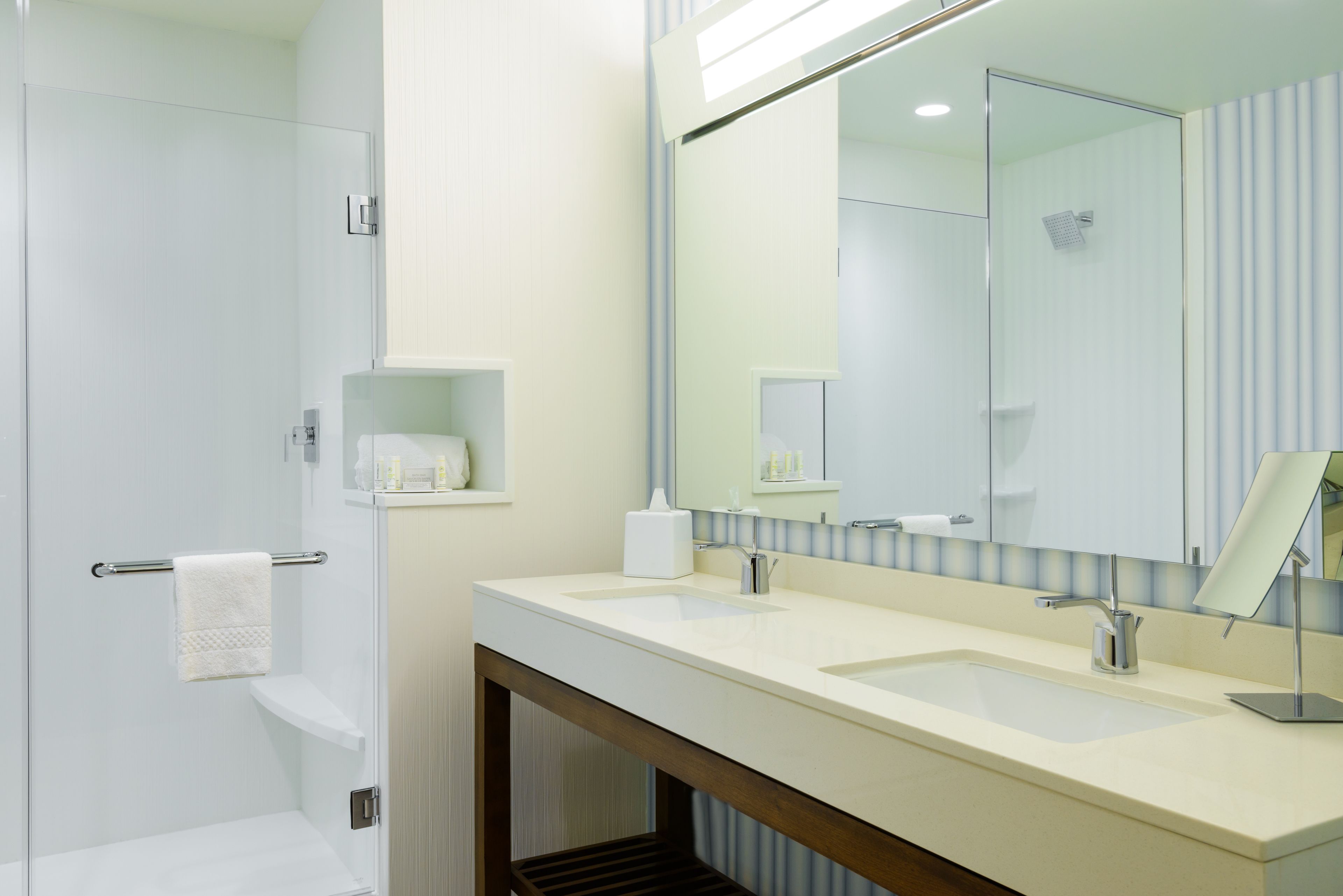 Une salle de bain moderne dotée d’une douche à parois de verre, d’un meuble-lavabo à deux vasques et d’un grand miroir.