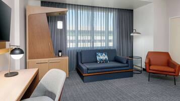 Una habitación de hotel moderna con sofá, sillón, escritorio y lámpara.