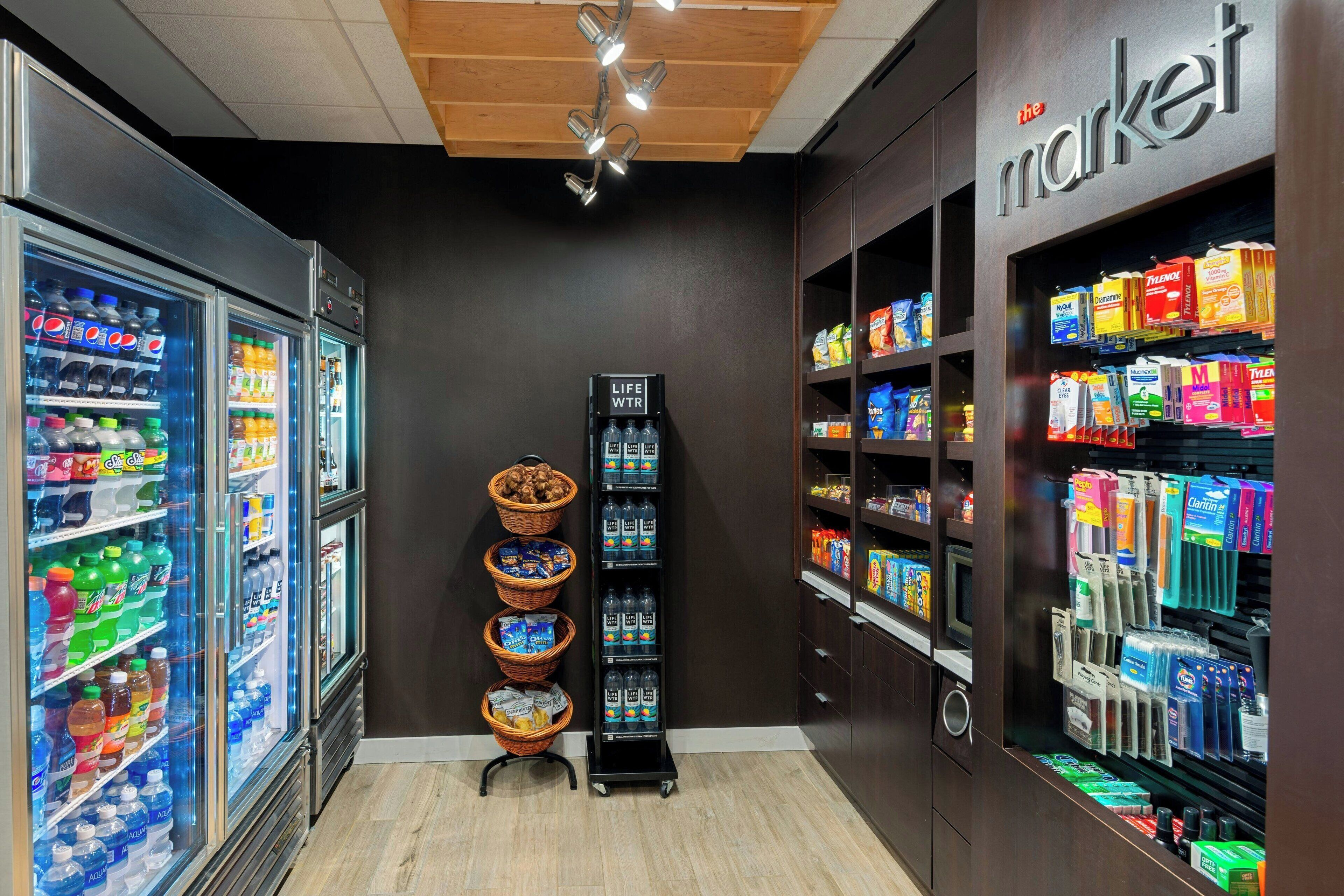 A grocery store interior with refrigerated beverage cases, a central display stand, and shelves stocked with various products.