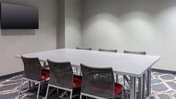 Una sala de conferencias con una larga mesa, seis sillas y un televisor de pantalla plana en la pared.