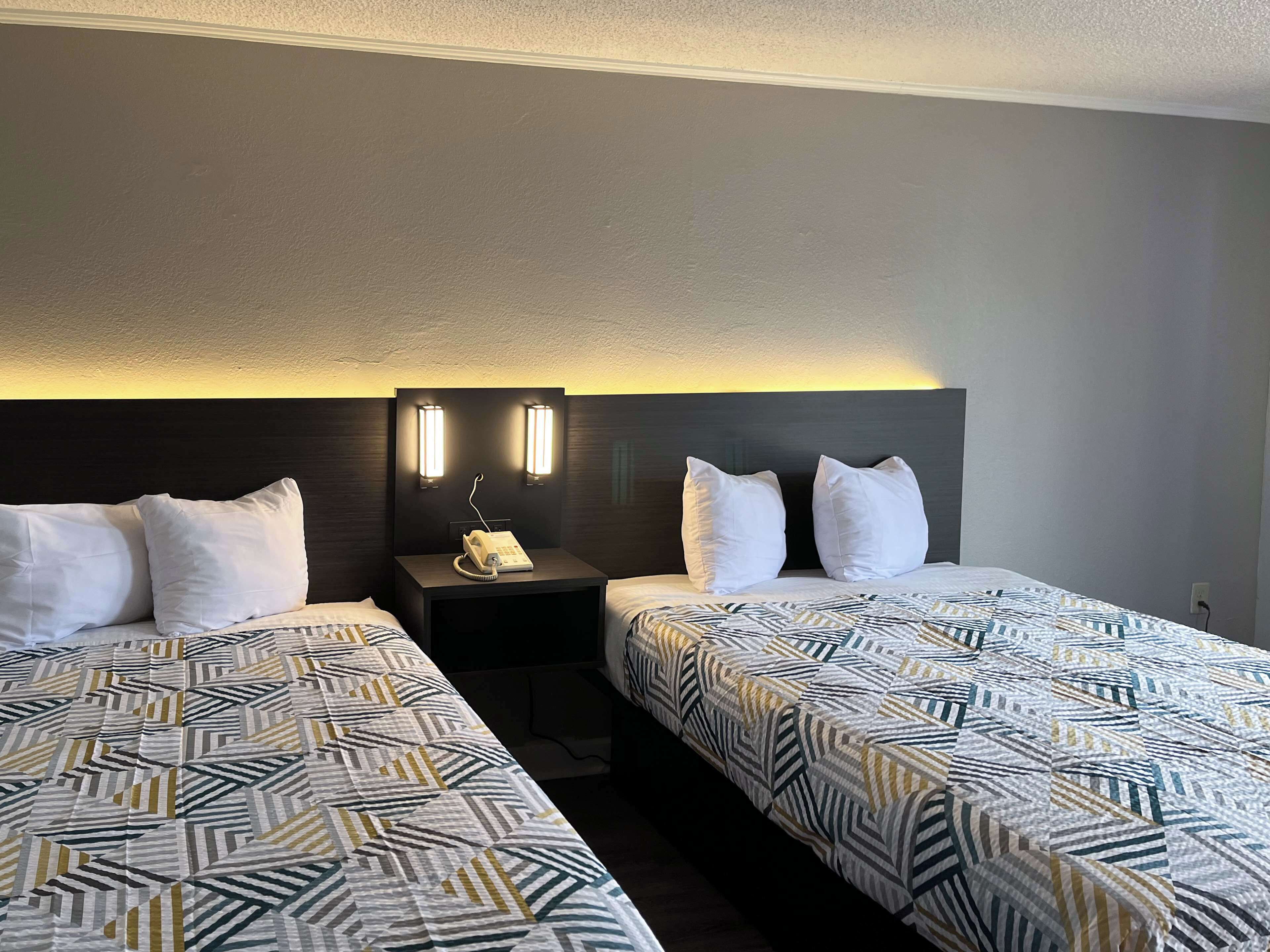 A hotel room with two beds, each with a patterned bedspread, a bedside table with a phone, and two wall-mounted lights.