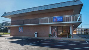 Un motel con un llamativo letrero que dice '6 Office', un estacionamiento y fachada de ladrillo.
