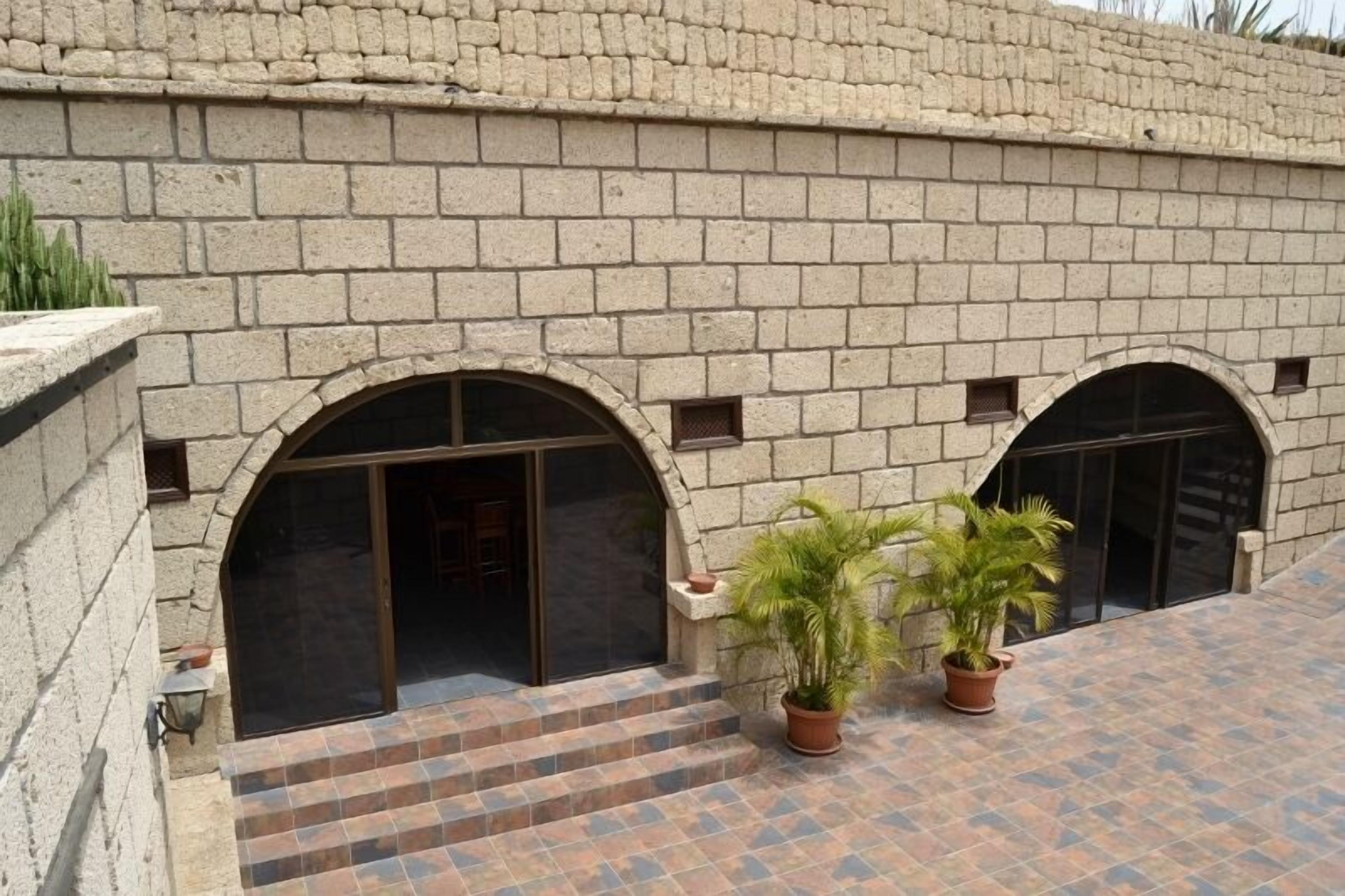 A courtyard with a stone wall, two arched doorways, and potted plants.
