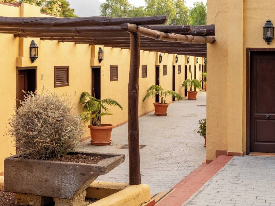 A courtyard with a wooden pergola, potted plants, and a door.