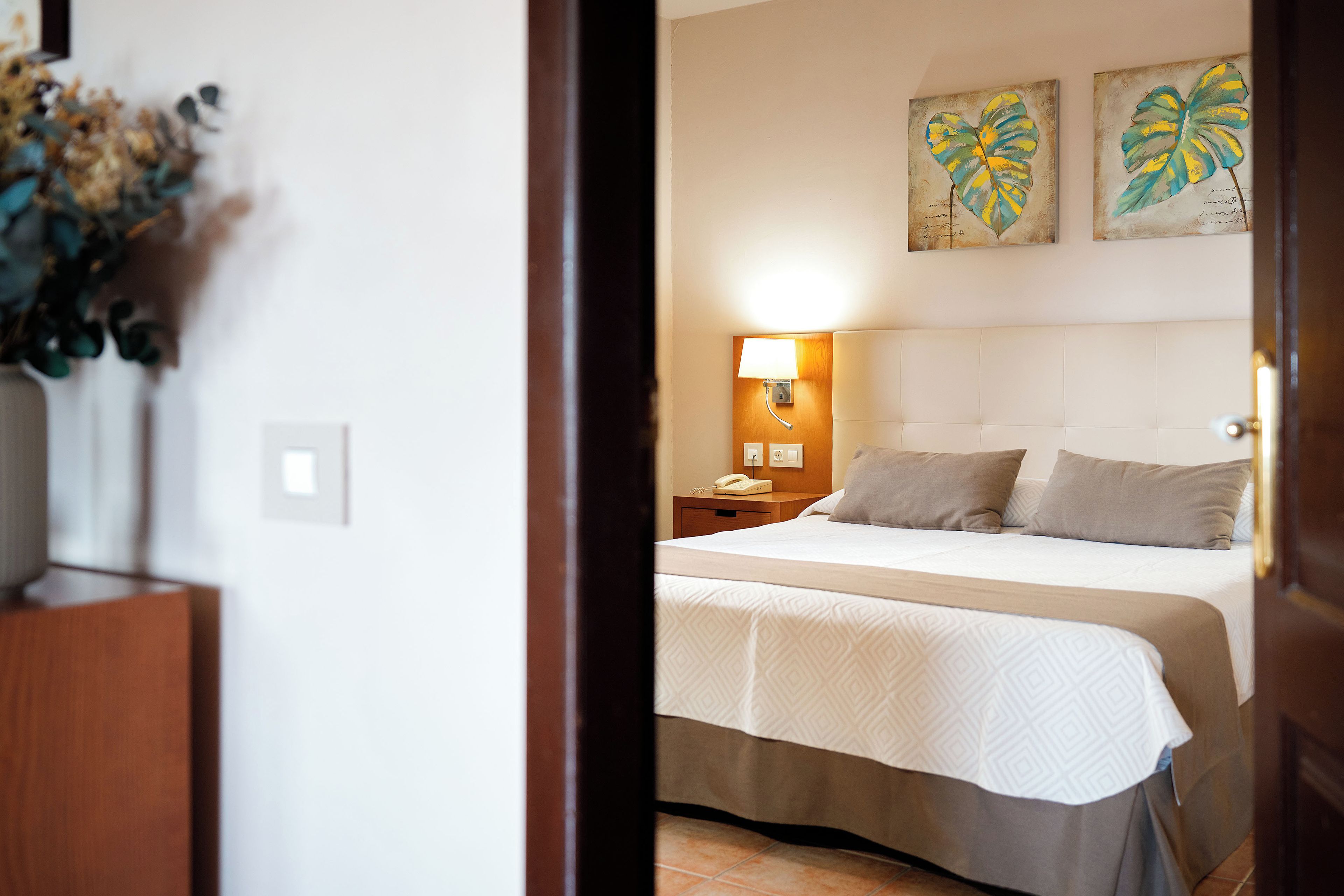 Habitación de hotel con cama, mesita de noche, lámpara y dos obras de arte colgadas en la pared.