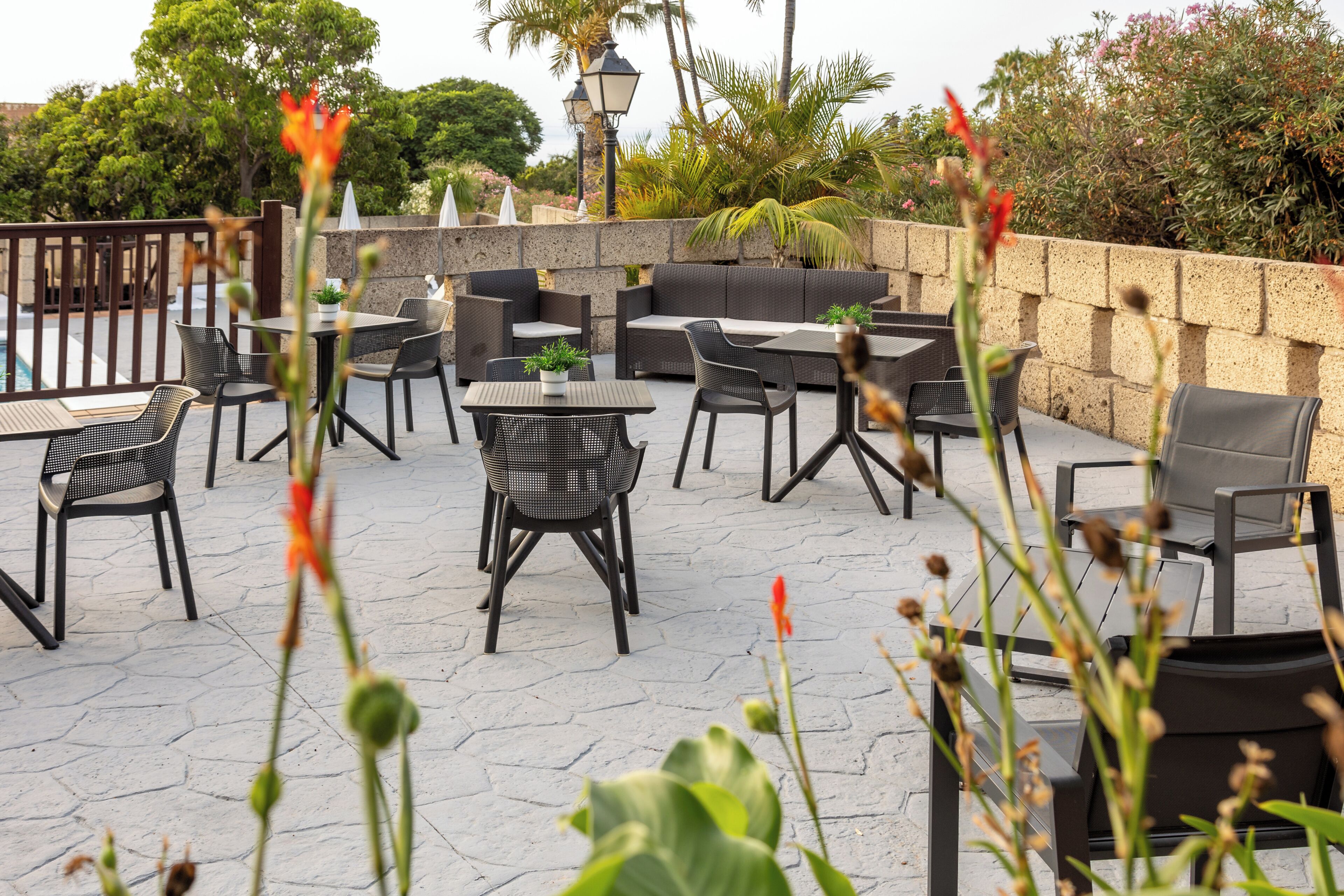 An outdoor seating area with tables and chairs, a stone wall, and potted plants.