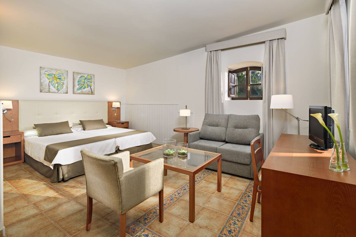 Une chambre d’hôtel comprenant un lit, deux tables de chevet, un canapé, une télévision et une petite table agrémentée d’objets décoratifs.