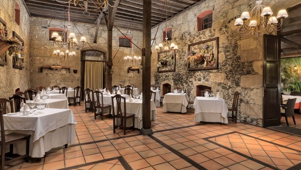 A restaurant with multiple tables and chairs, stone walls, and hanging chandeliers. - Hotel Rural Finca Salamanca (Güímar)