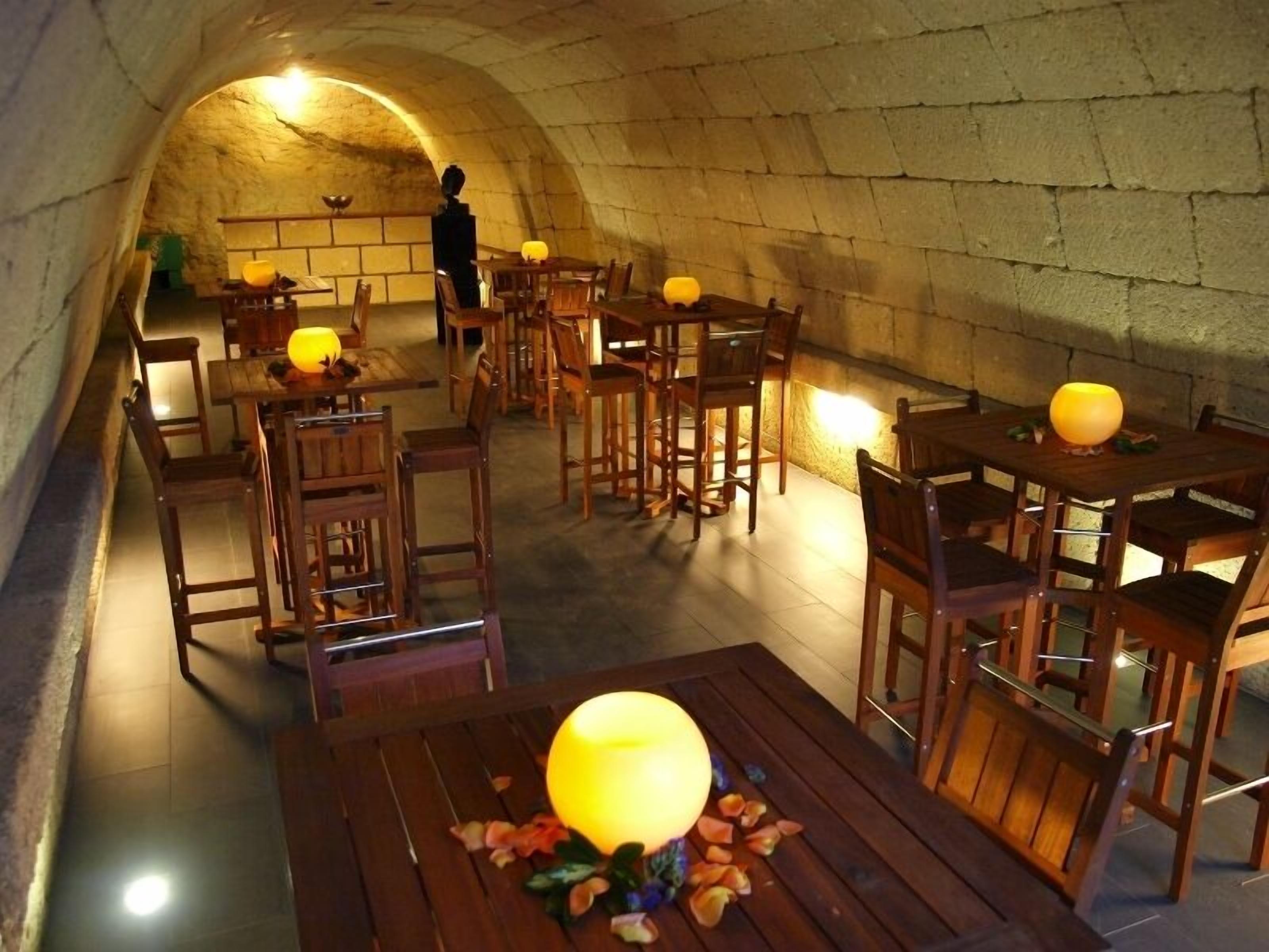 Un espace de restauration souterrain avec des murs en pierre, des tables et des chaises en bois, et des lampes de table.