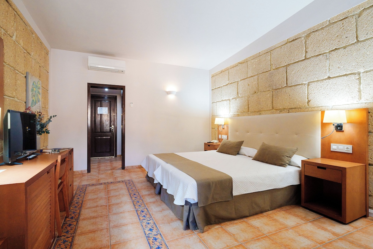 A hotel room with a bed, bedside tables, a desk with a television, and a decorative wall.
