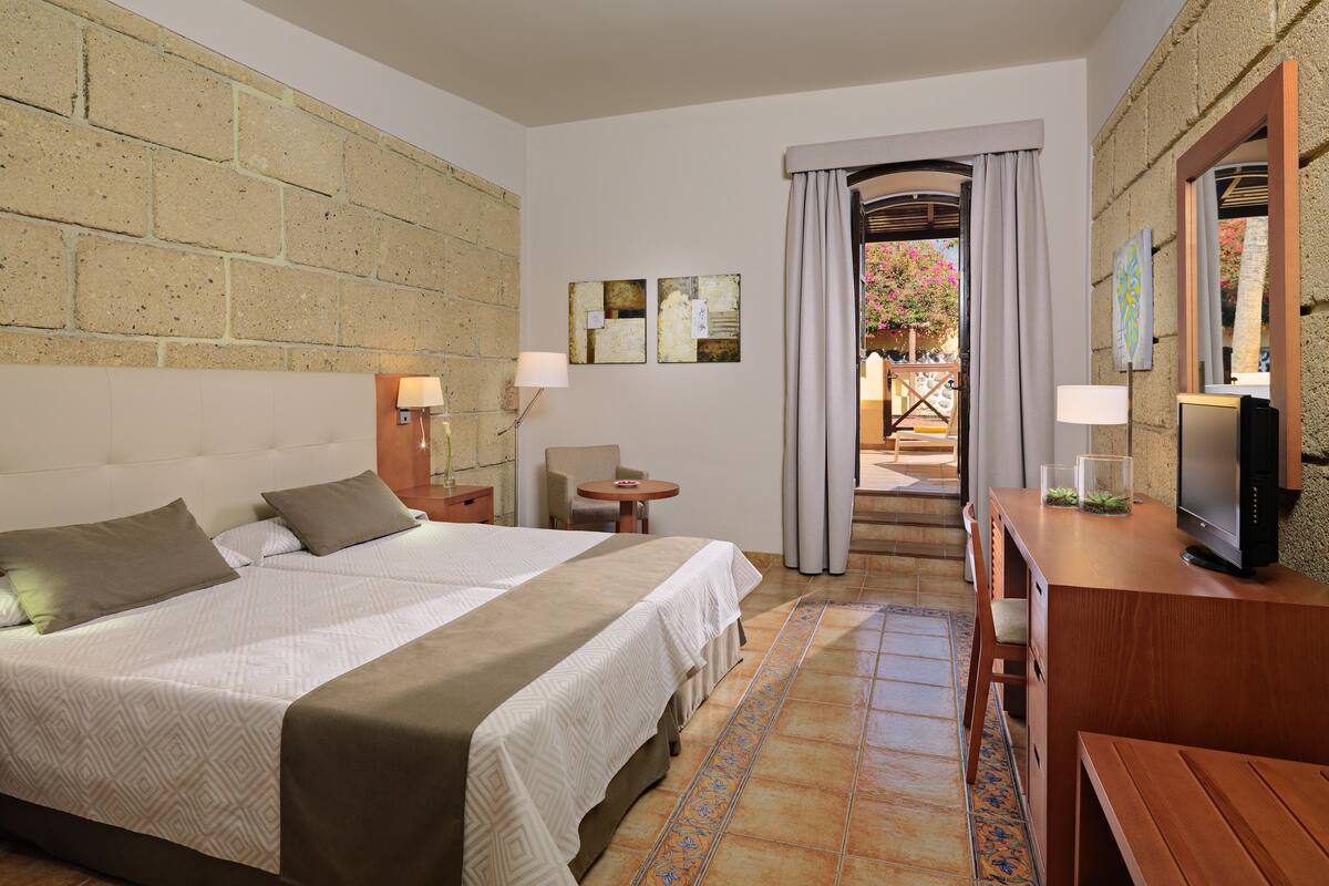 Une chambre d’hôtel avec un grand lit, un bureau avec un ordinateur, une chaise et une petite table sur laquelle se trouve un vase.