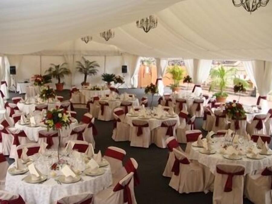 Un espacio para eventos con carpas, mesas redondas, manteles blancos y cintas rojas.