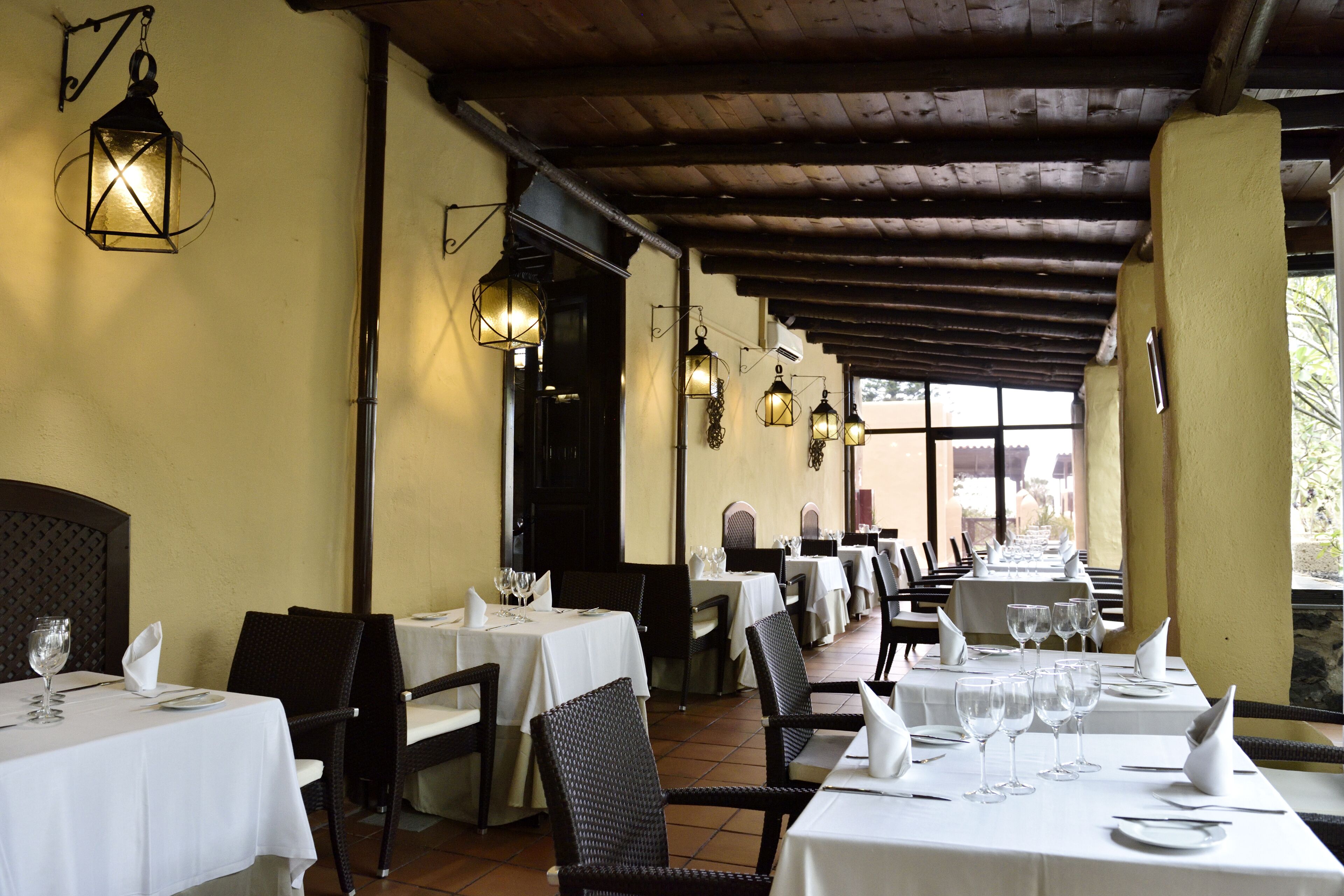 Een restaurant met meerdere tafels gedekt voor diners, met witte tafelkleden en zwarte rieten stoelen.