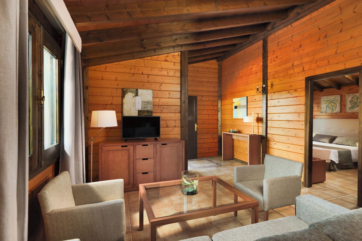 A cozy cabin-style room with a wooden interior, a television on a cabinet, a glass-top coffee table, and a sofa.