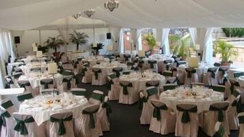 A tented event space with round tables, each with a white tablecloth and green sashes, and chairs with matching sashes.