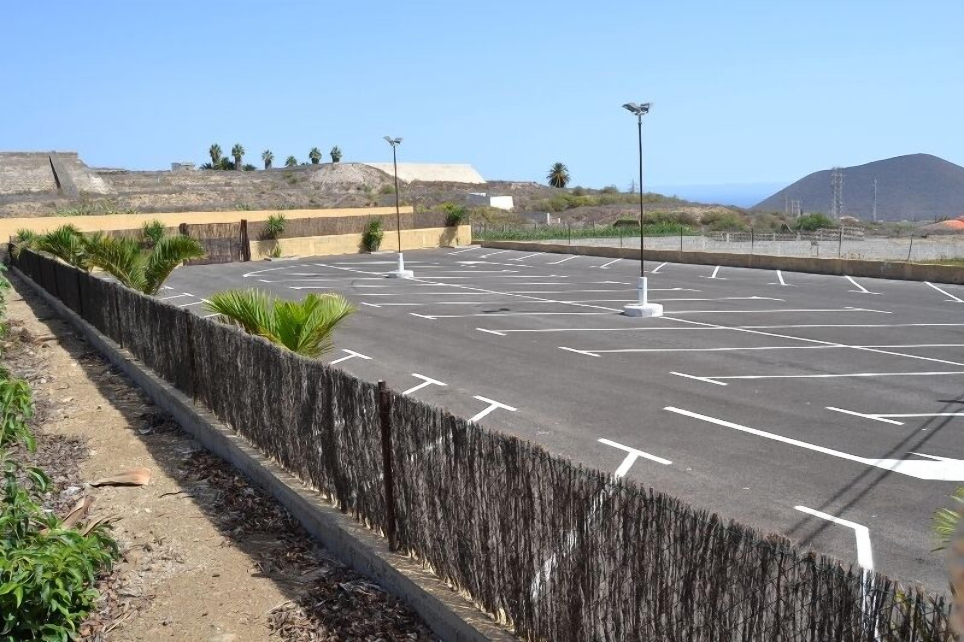A parking lot with marked spaces, a fence, and a mountainous backdrop.