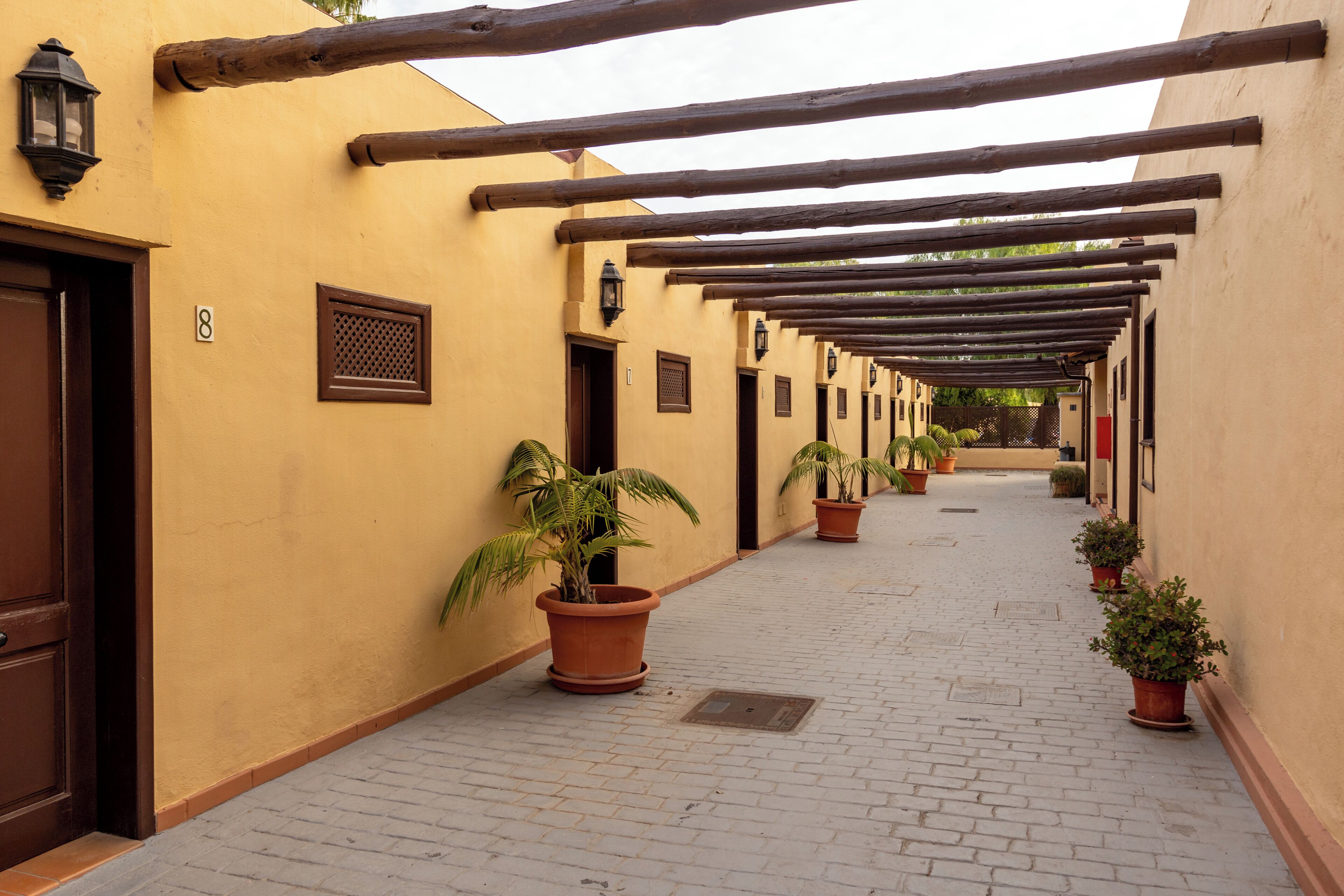 A corridor with wooden beams, potted plants, and doors with numbers.