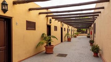 A corridor with wooden beams, potted plants, and doors with numbers.