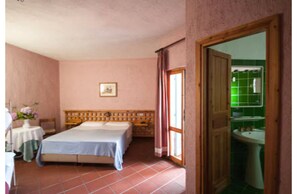 A bedroom with a bed, a small table with a vase of flowers, and a view of a bathroom through an open door. - Hotel Scintilla (San Teodoro)