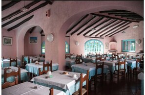 A dining area with tables and chairs, arched ceilings, and a pink wall. - Hotel Scintilla (San Teodoro)