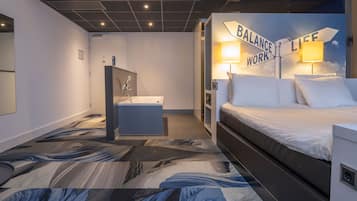A hotel room with a bed, a desk, a sink, and a shower area.