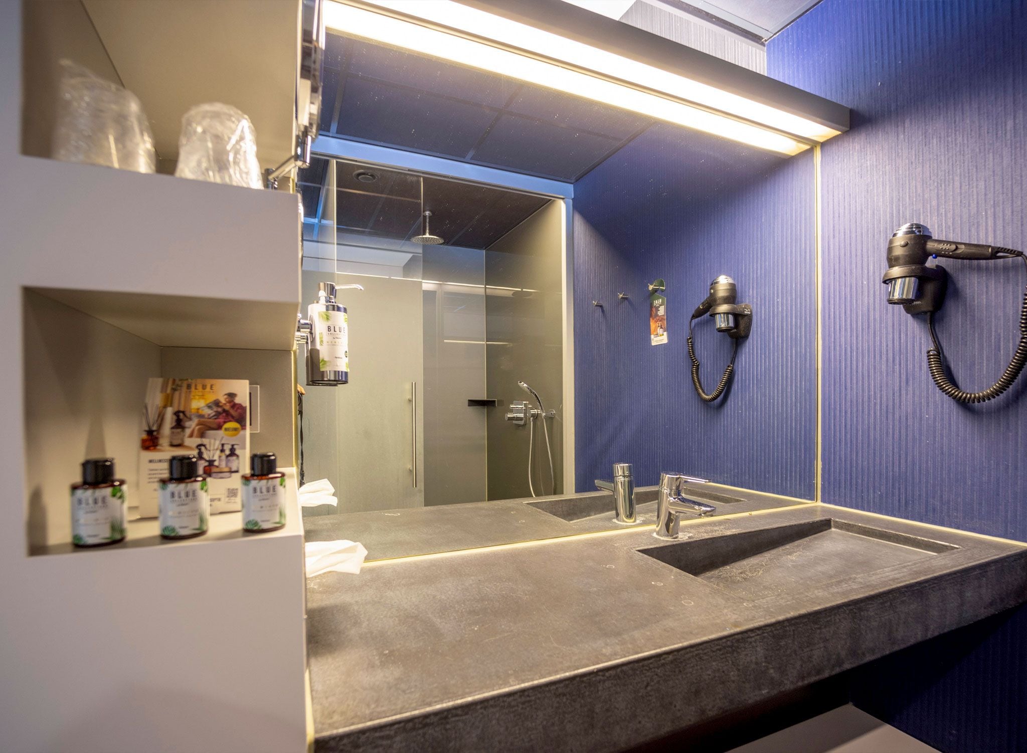Un baño moderno con un espejo grande, un lavabo y un secador de pelo montado en la pared.