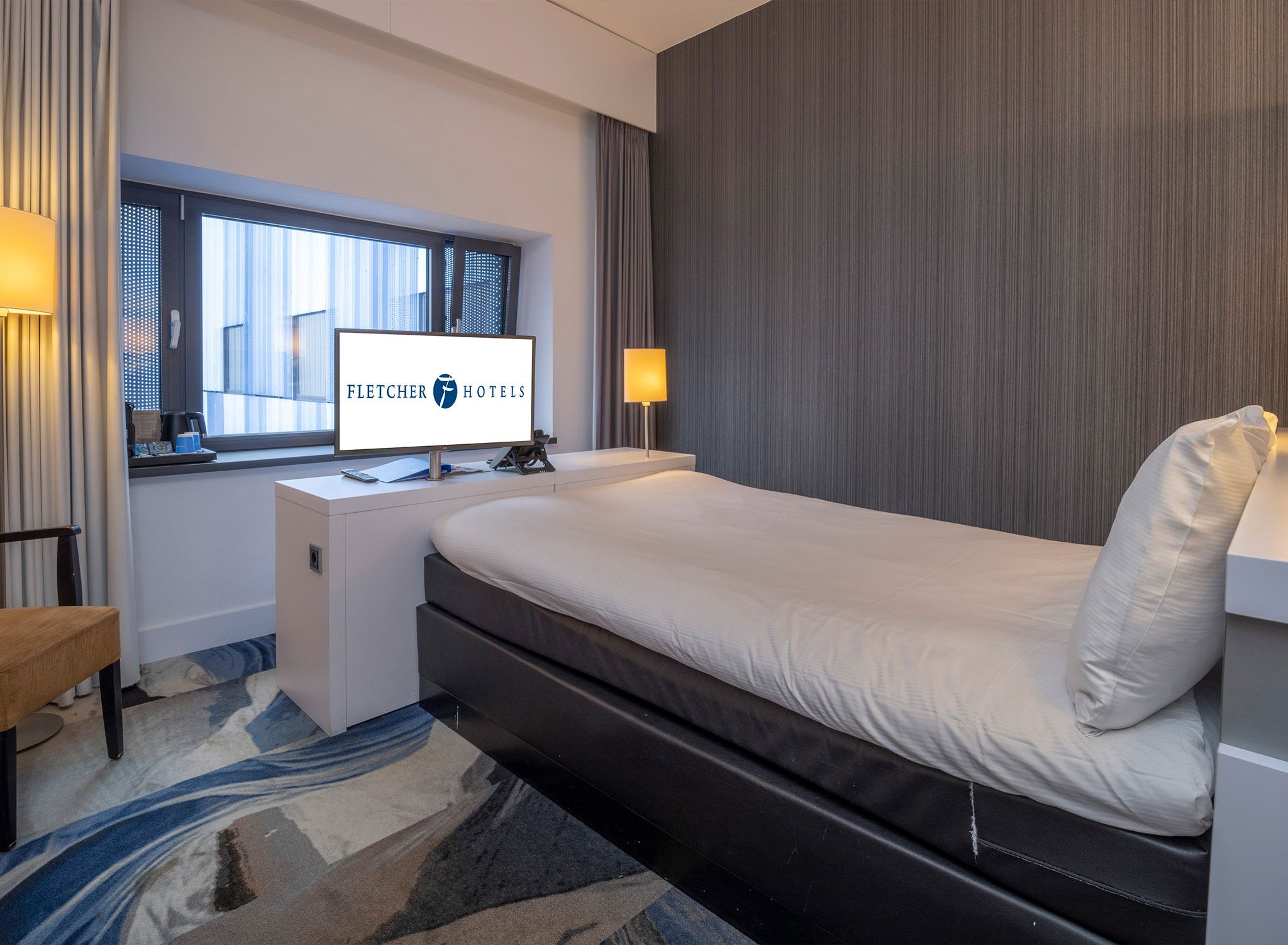 A hotel room with a bed, desk, and a window with curtains.
