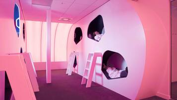 Quarto com paredes rosa, várias janelas circulares e mobiliário branco.