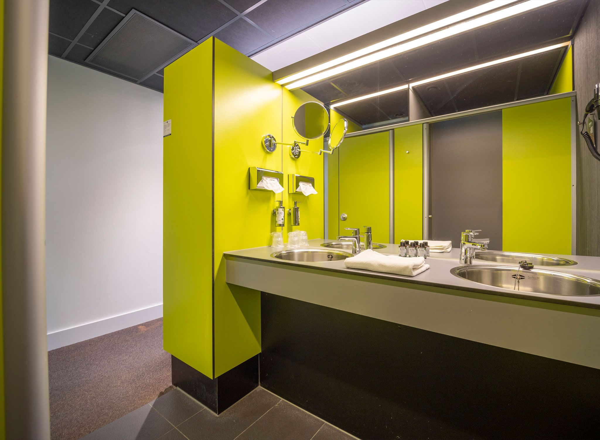 Un baño moderno con dos lavamanos, un espejo y paredes de color verde brillante.