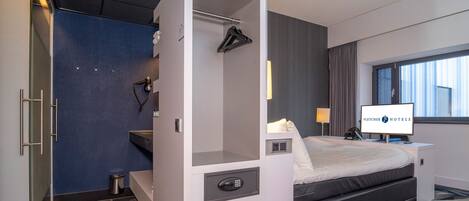 A modern hotel room with a bed, a desk with a chair, a bathroom, and a window with curtains.