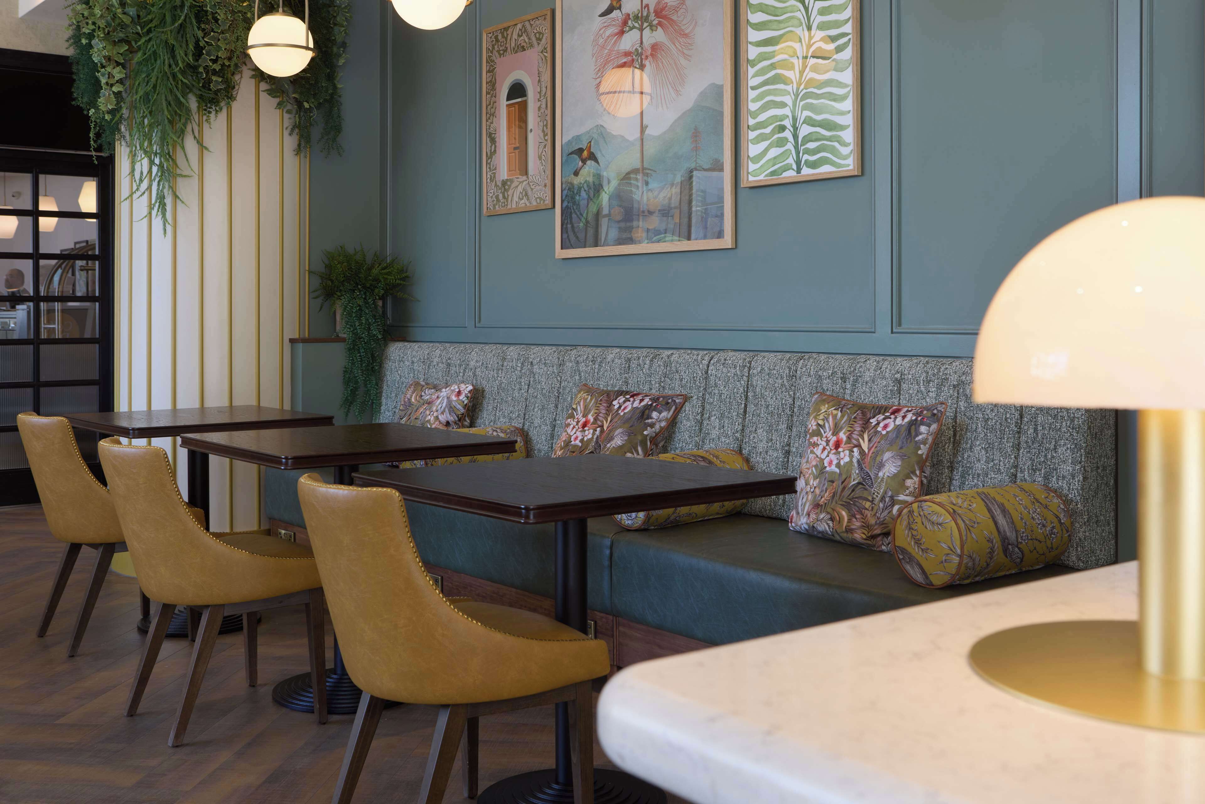 Un restaurant avec des tables et des chaises en bois, un banc vert rembourré et des œuvres d’art murales.