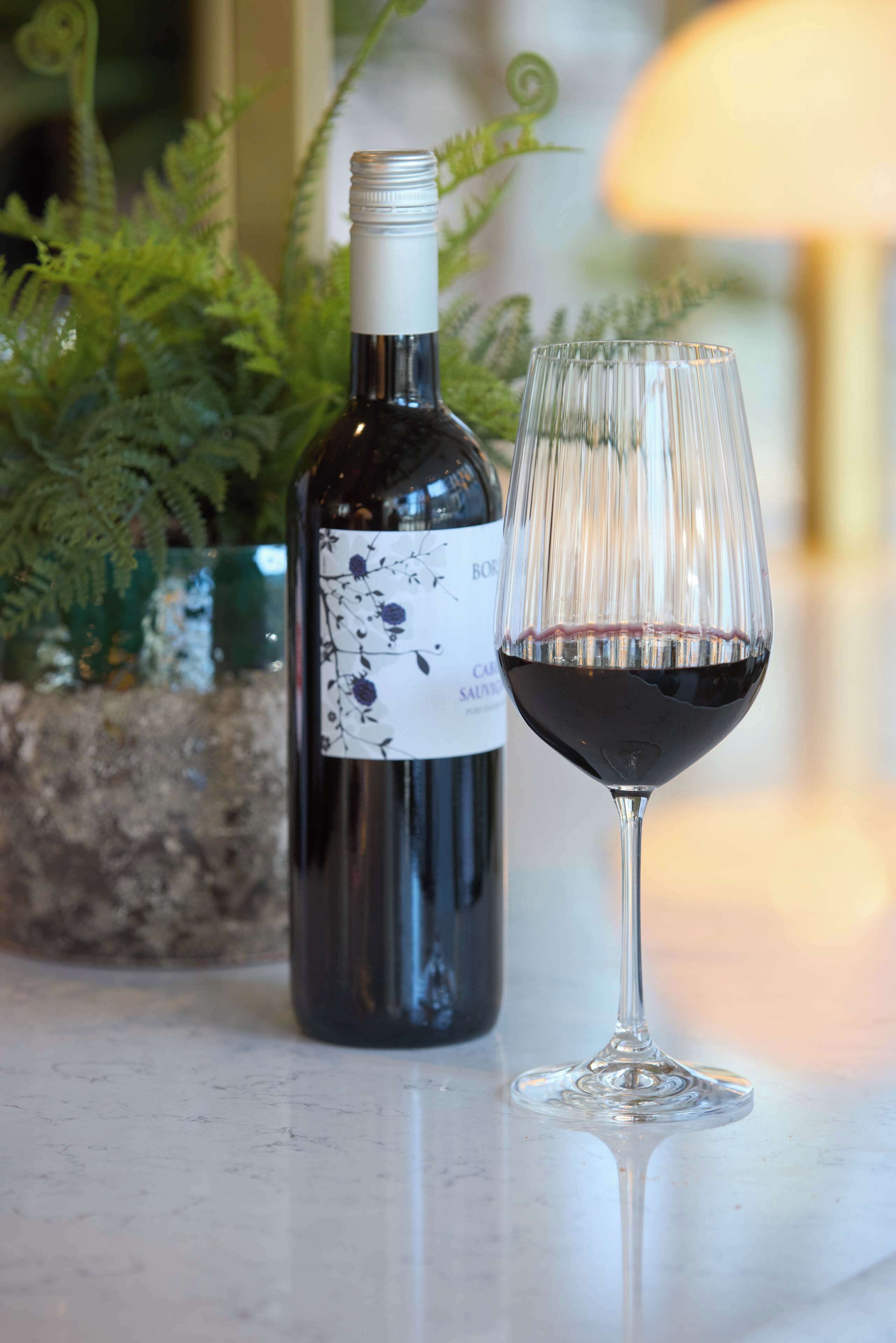 A bottle of wine and a glass of red wine on a marble surface.
