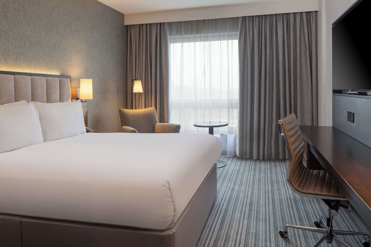 A hotel room with a large bed, a desk, a chair, a TV, and a small table.