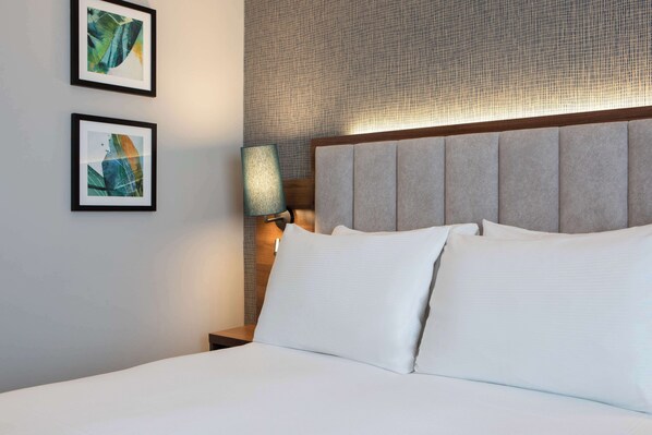 A neatly made bed with white linens, a headboard with a textured panel, and two framed abstract artworks on the wall.