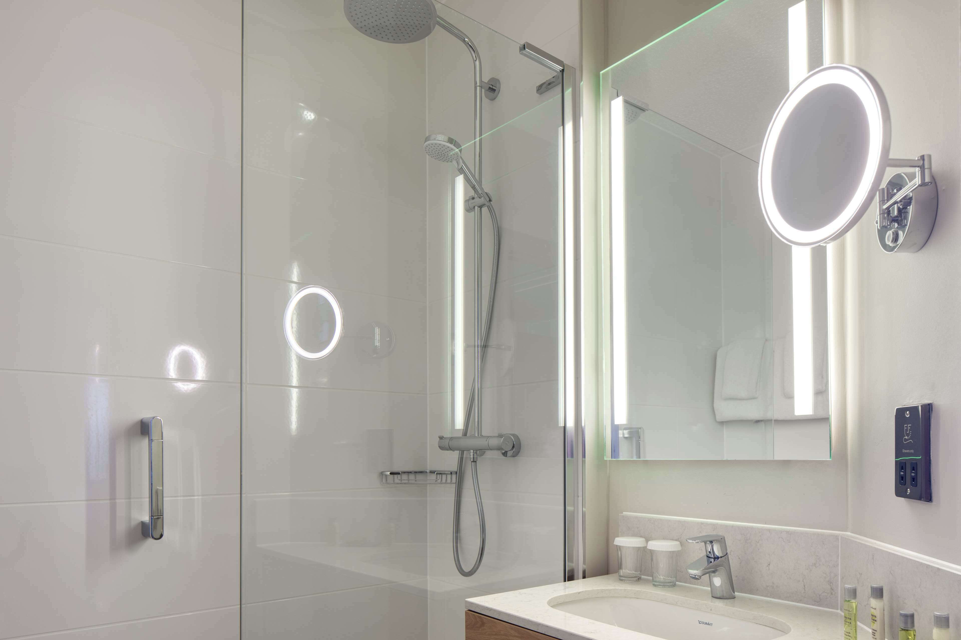 Une salle de bain moderne avec une douche à parois de verre, un meuble-lavabo avec un miroir et un luminaire fixé au mur.