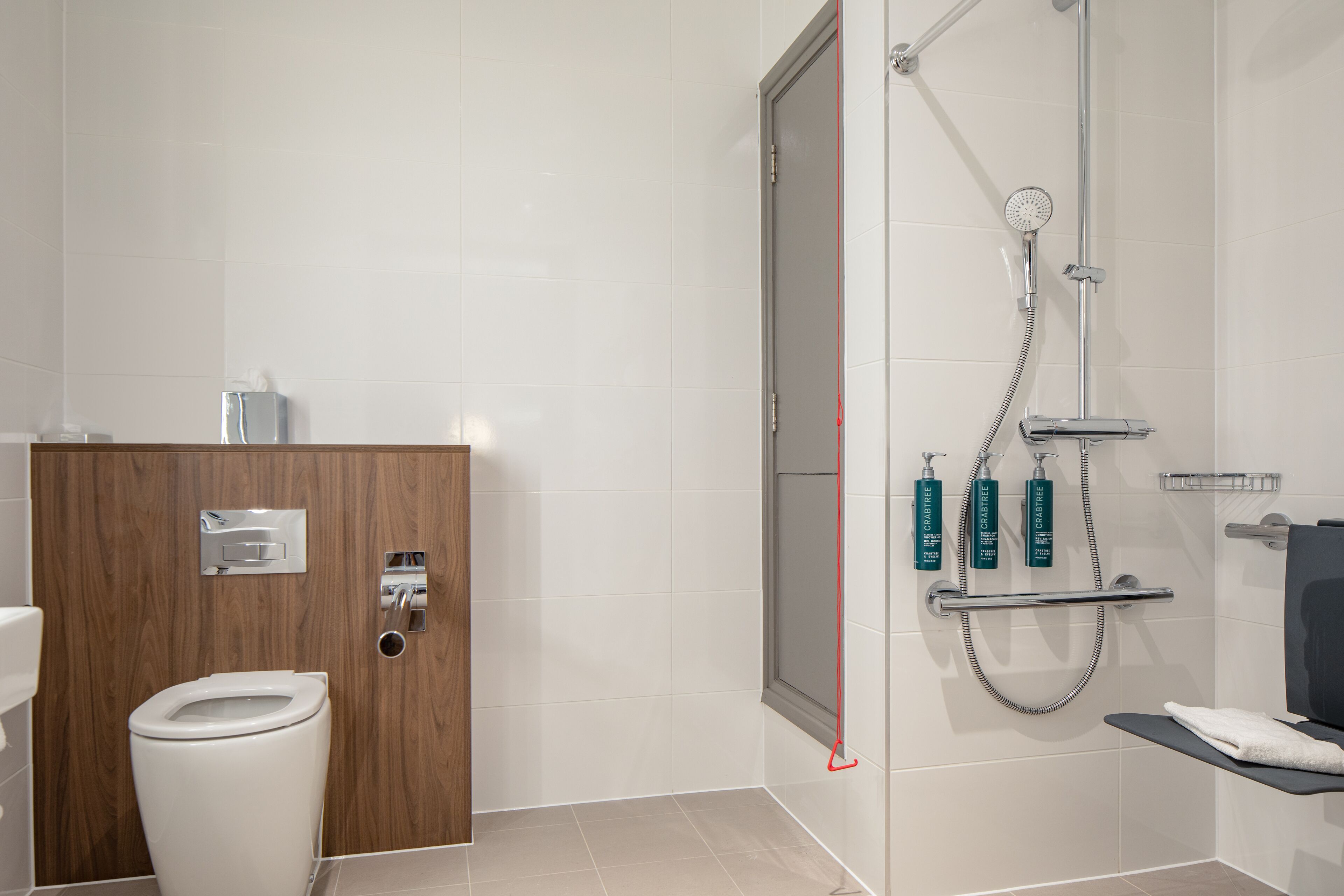 Een moderne badkamer met toilet, douche met handdouche en een handdoekrek.