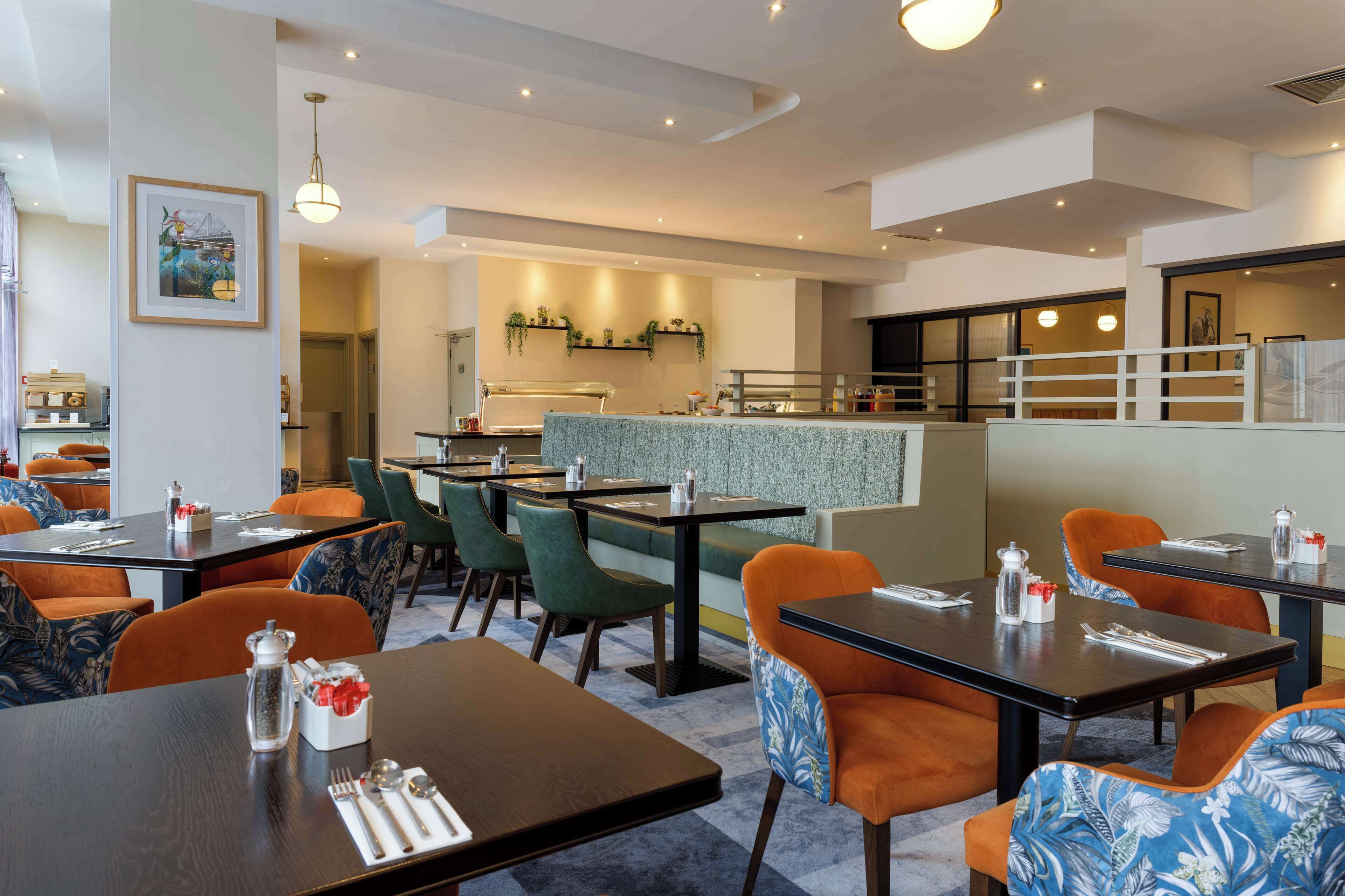 A modern restaurant with multiple dining tables and chairs, a kitchen area, and a bar.
