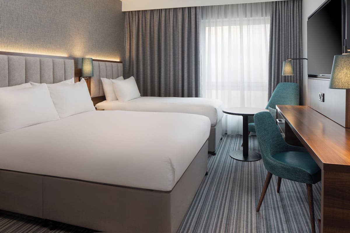 A hotel room with a large bed, a smaller bed, a desk, a chair, and a TV.