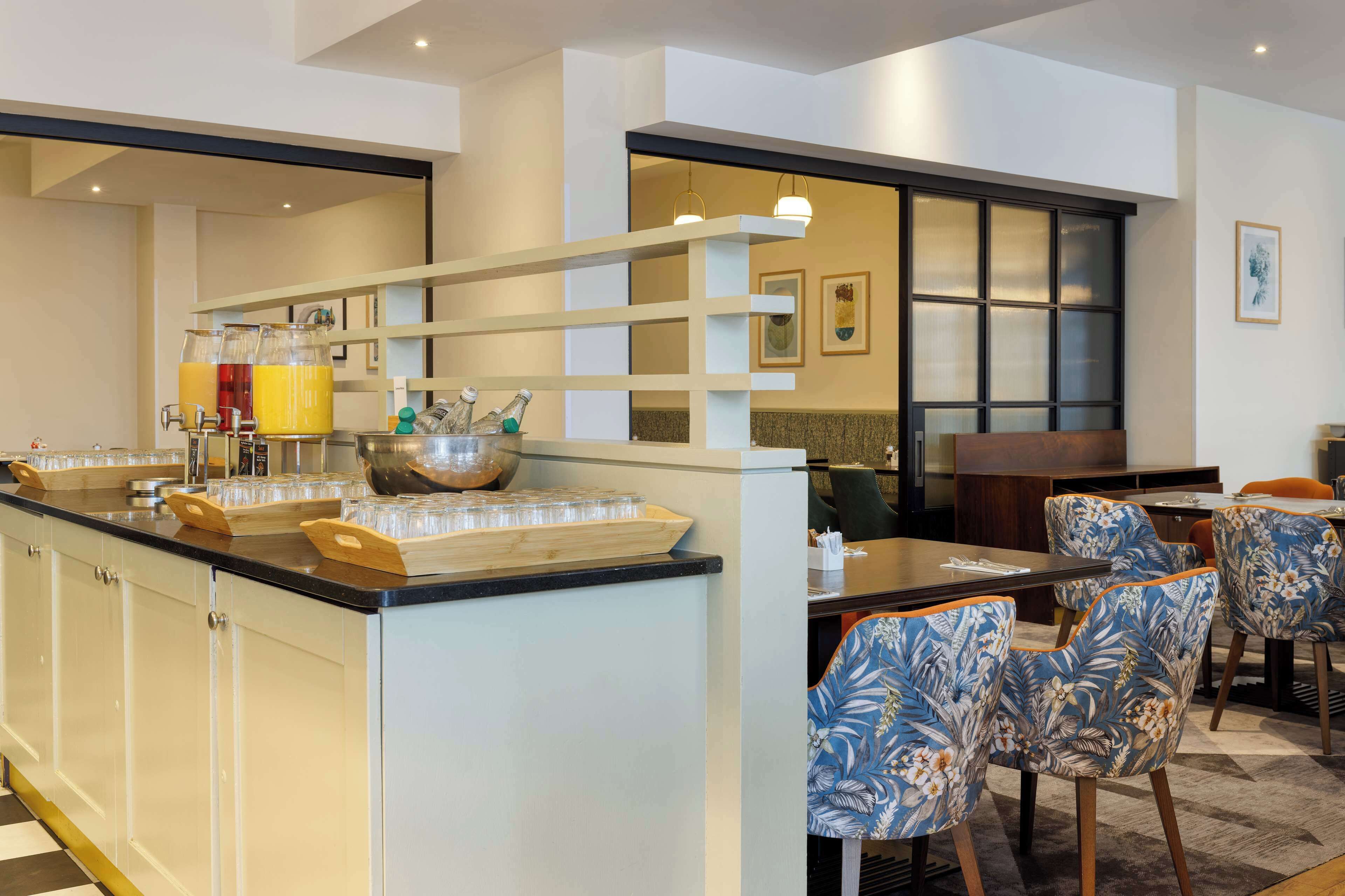 A breakfast bar with juice dispensers, a buffet area, and a seating area with patterned chairs.